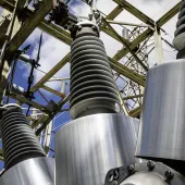 Close-up view of high-voltage transformer equipment at an electrical substation, showcasing metal insulators and power grid infrastructure against a blue sky for energy industry use.