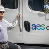 A worker in a hard hat and uniform stands beside an AES Ohio truck, holding the door handle. The truck displays the AES Ohio logo.