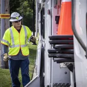 AES Ohio lineworker in high-visibility safety gear stands beside a utility truck with traffic cones, preparing for field operations on a sunny day.