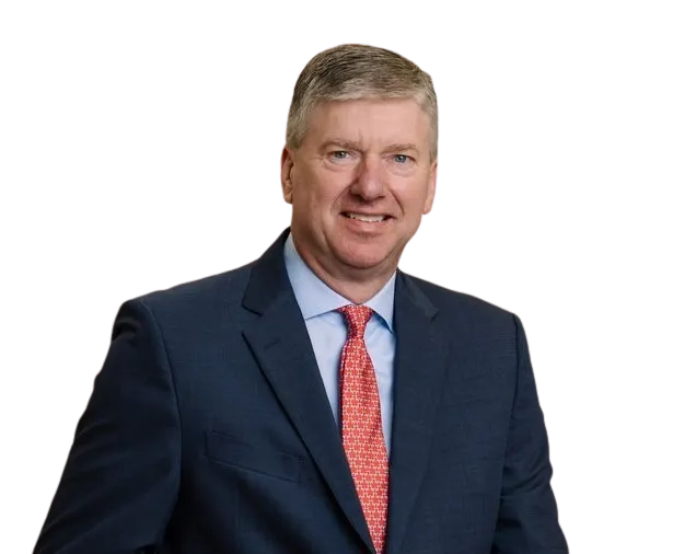 Smiling middle-aged man wearing a dark blue suit, light blue shirt, and red patterned tie, posing against a plain background.