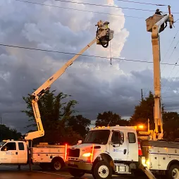 Dark storm clouds over a coastal road with wet pavement, faint industrial structures in the distance, and a power line cutting across the sky.